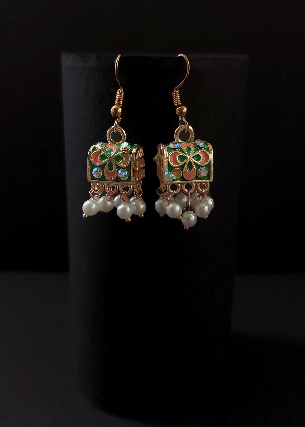 Pair of earrings with decorative elements and pearl-like beads on a black background