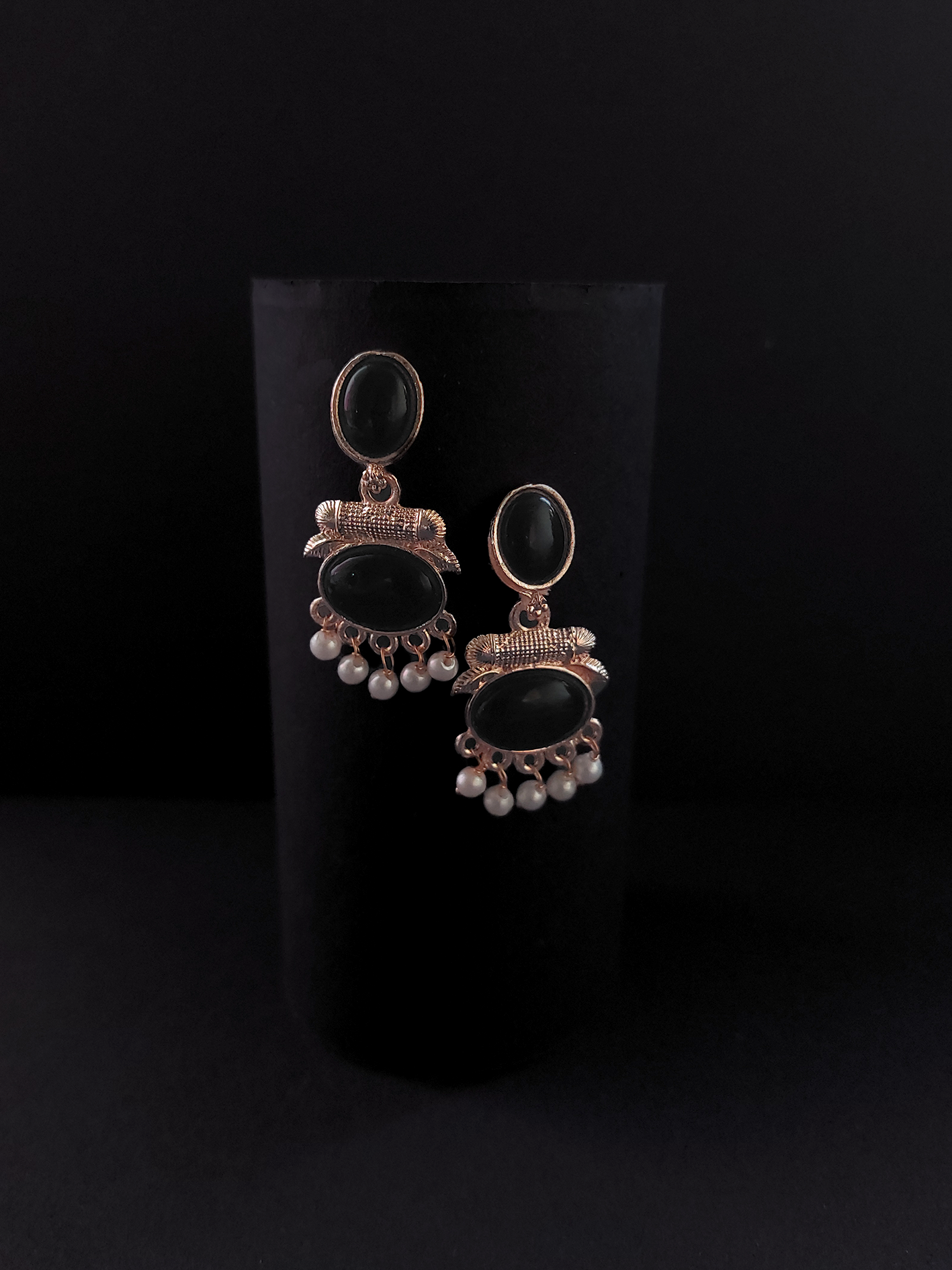 Pair of earrings with black stones and pearl-like beads on a black background