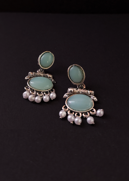 Pair of earrings with green gemstones and pearl-like beads on a black background