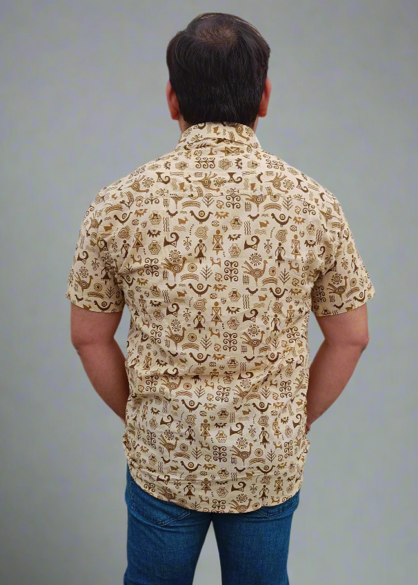 Man wearing a patterned beige shirt and blue jeans on a gray background