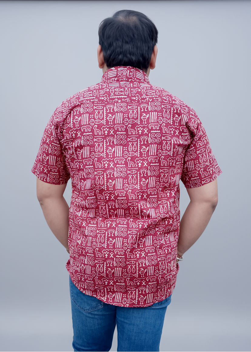 Person wearing a red patterned shirt and blue jeans standing against a plain wall.