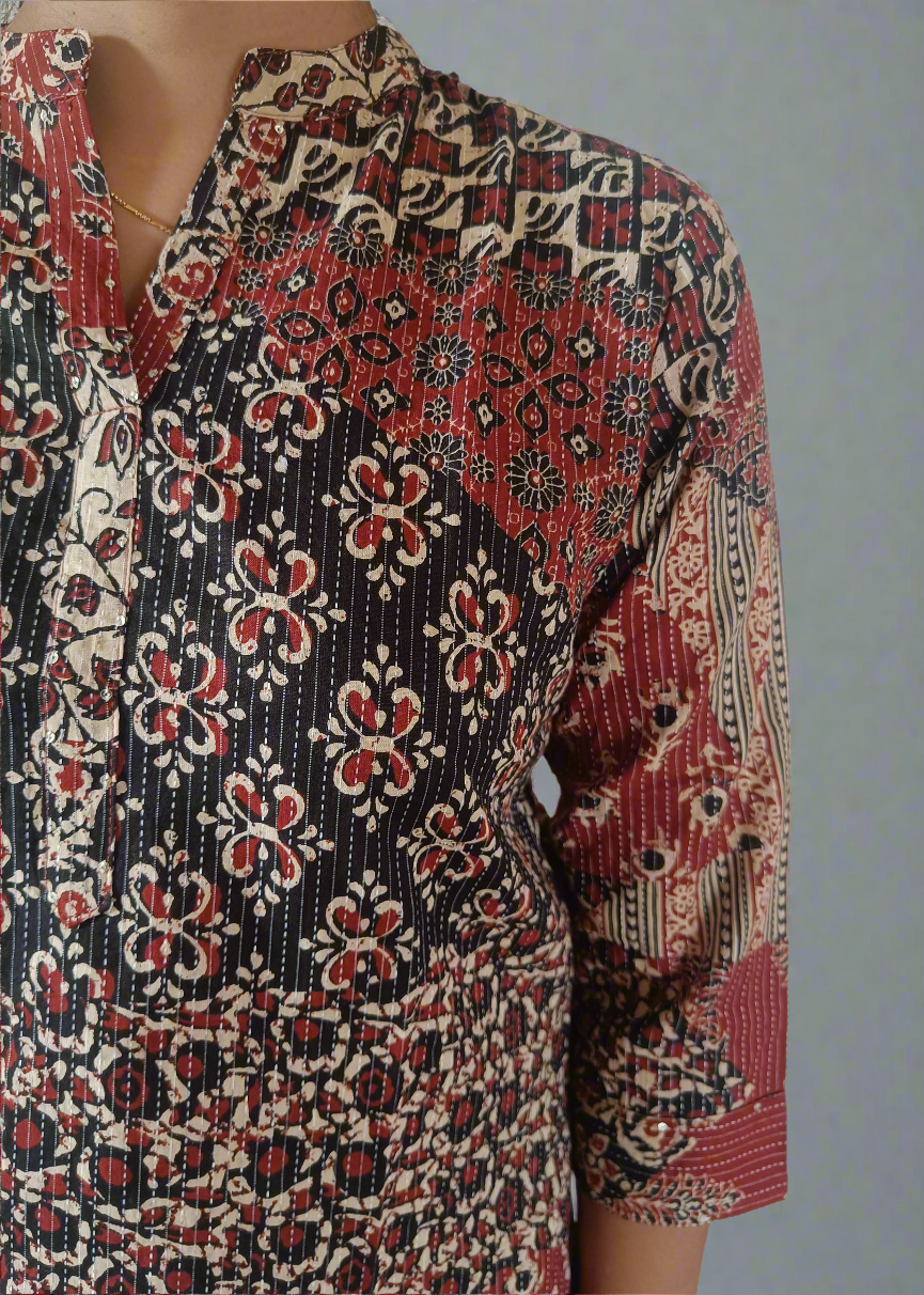 Close-up of a patterned tunic shirt top with red, black, and white colors on a neutral background