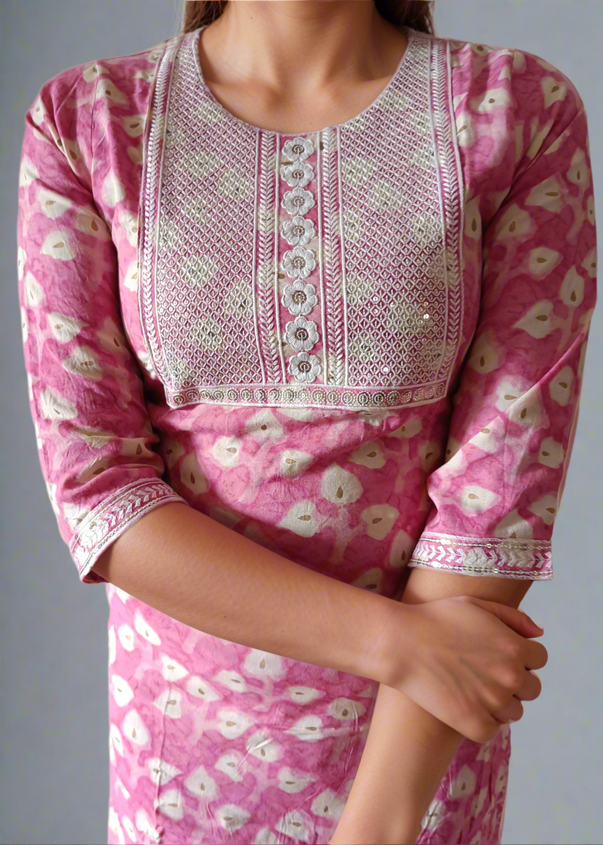 Pink traditional outfit with white floral patterns and intricate detailing on a plain background