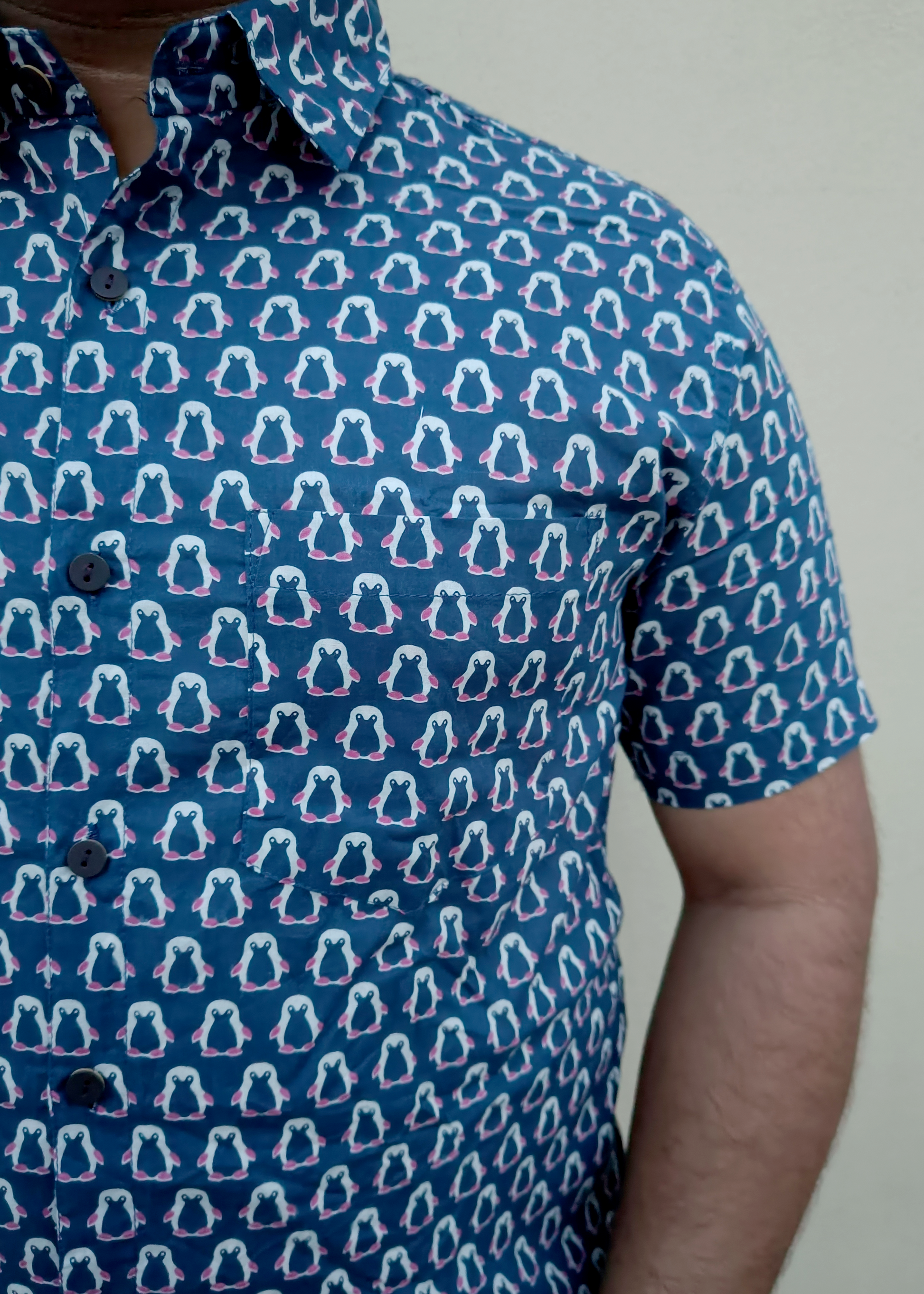 Blue shirt with penguin pattern worn by a person against a plain background
