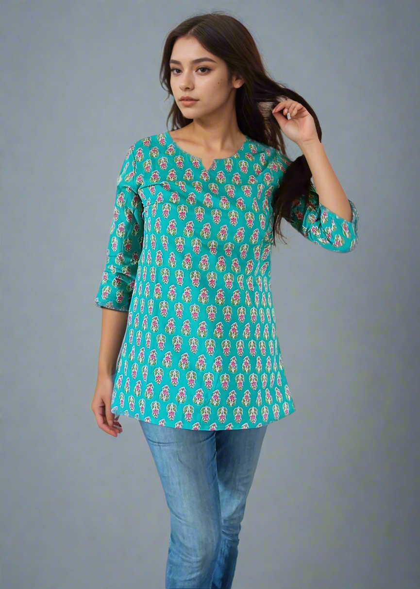 Woman wearing a green patterned top and blue jeans against a plain background