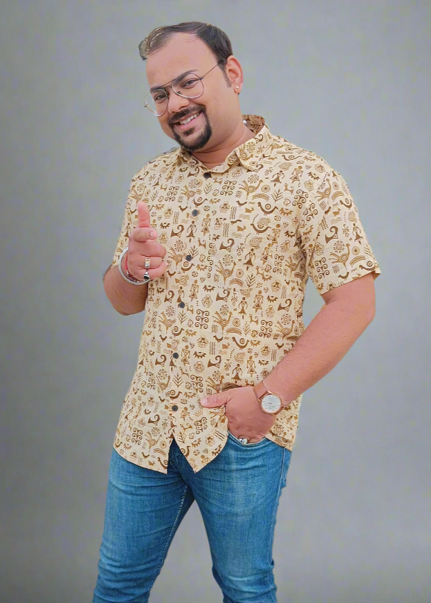 Man wearing a patterned shirt and blue jeans giving a thumbs-up gesture against a beige wall.