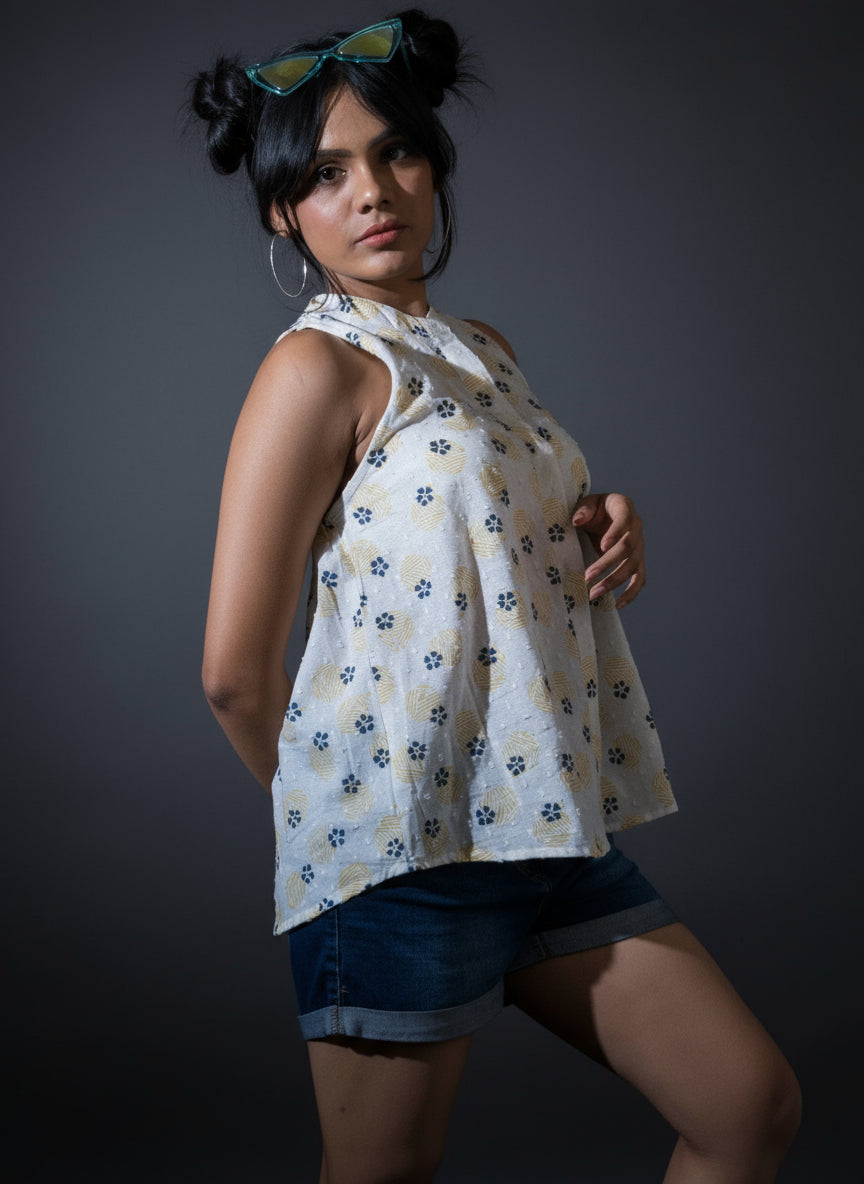 Woman wearing a floral top and denim shorts standing against a dark curtain.