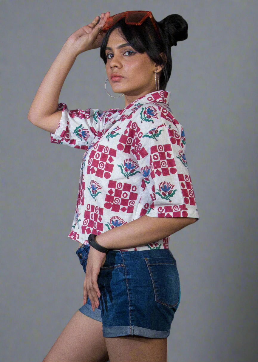 Woman wearing a floral top and denim shorts against a dark curtain background