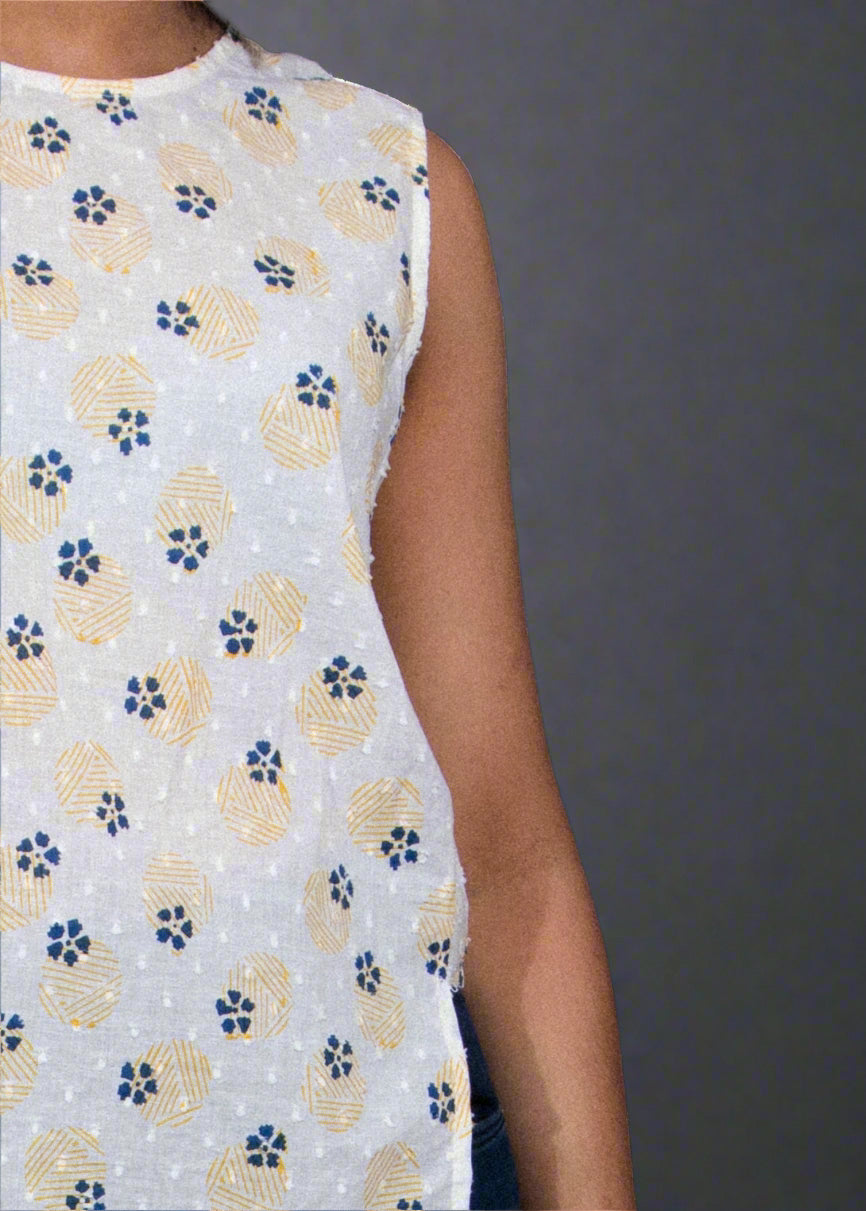 Woman wearing a white sleeveless top with floral pattern and blue jeans against a black background