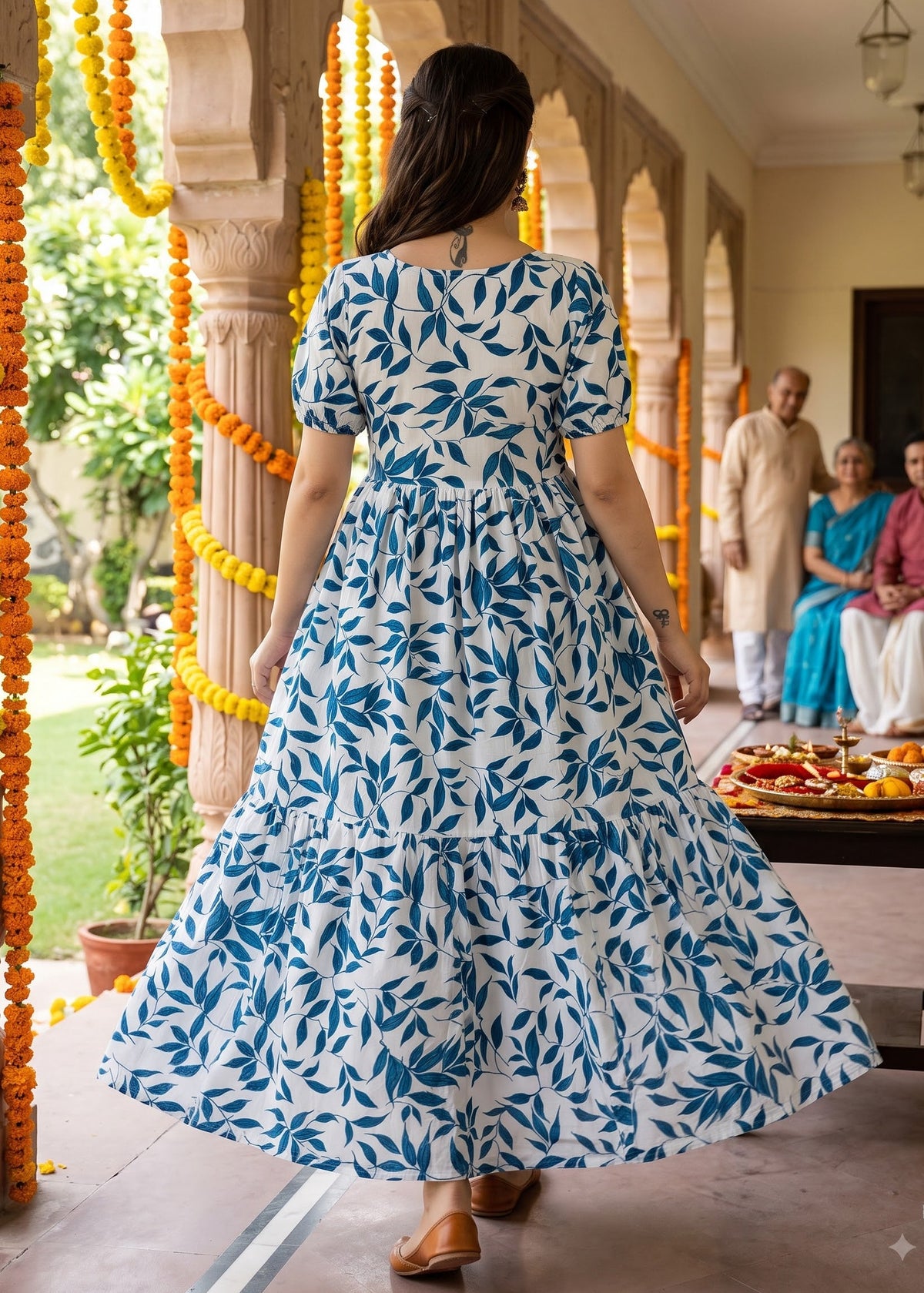 A woman wearing a blue and white patterned tiered maxi dress walks in a traditional courtyard decorated with yellow marigold garlands.