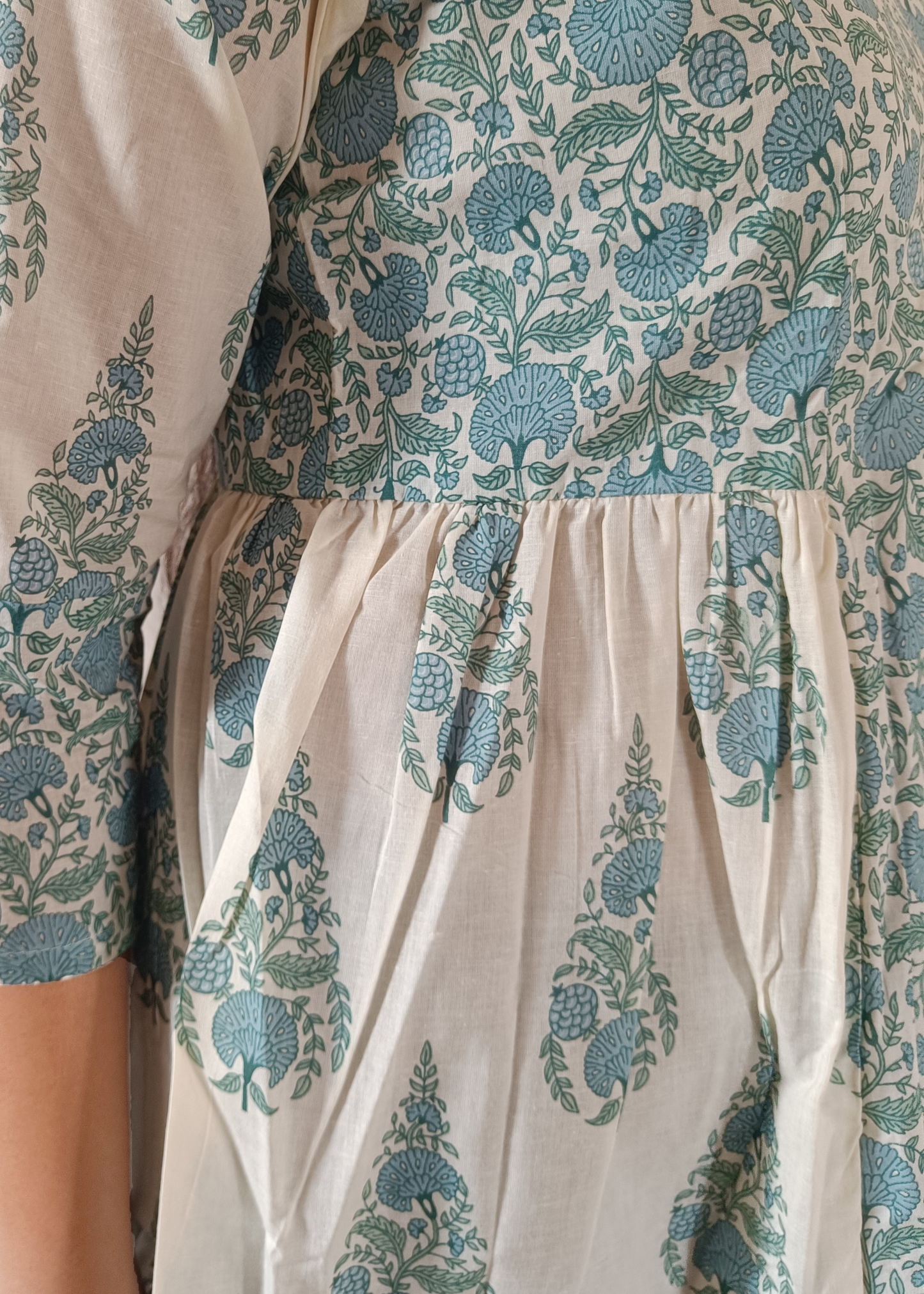 Woman wearing a patterned flroral paisley top and jeans on a plain background