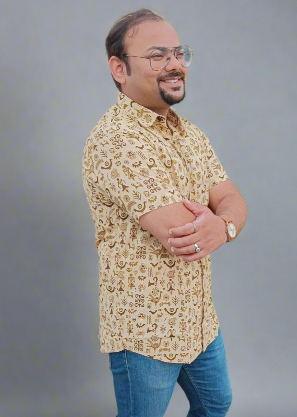 Man wearing a patterned shirt and jeans standing against a gray background