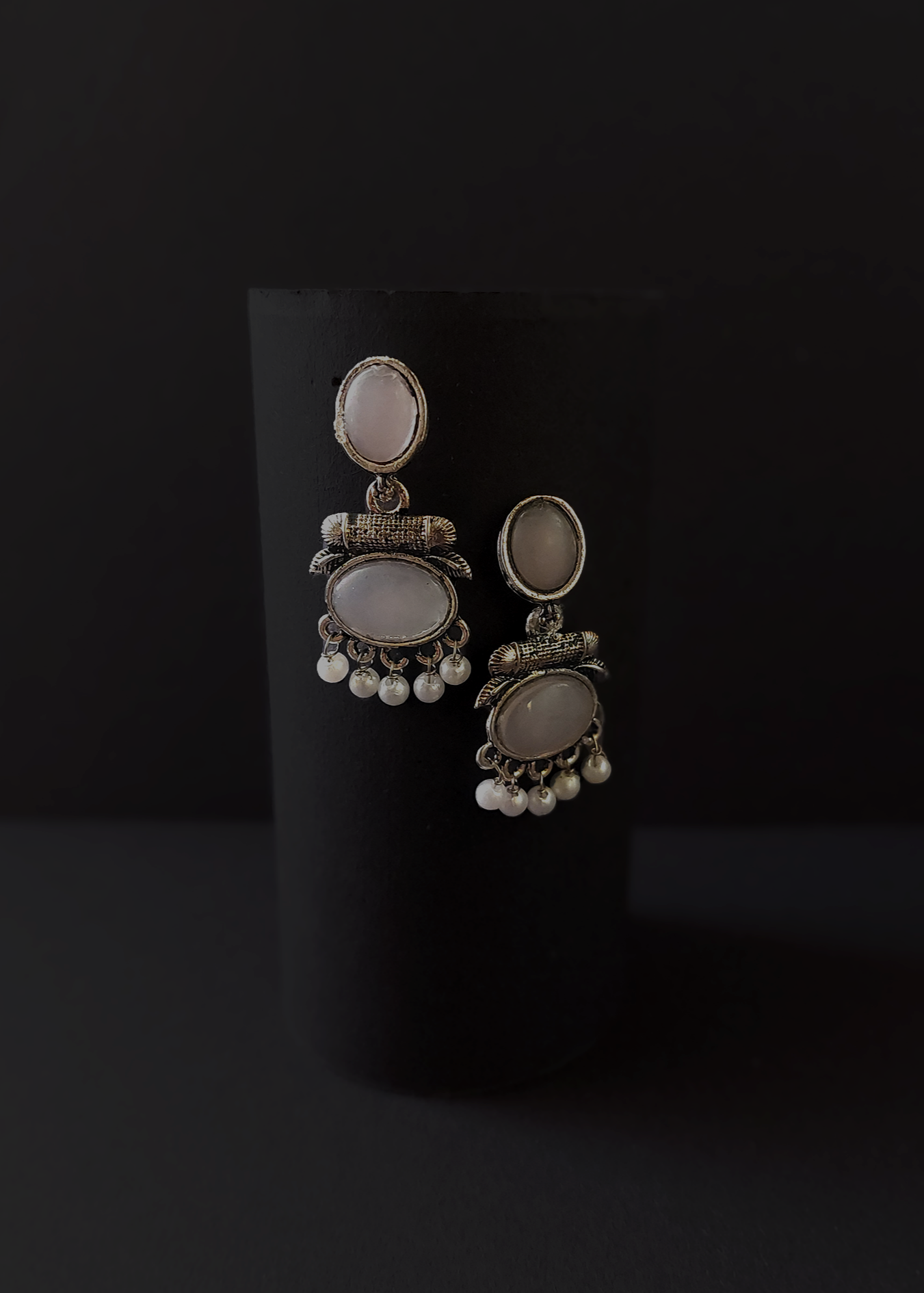 Pair of silver earrings with gemstones and pearls on a black background