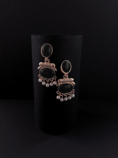 Pair of earrings with black stones and pearl-like beads on a black background