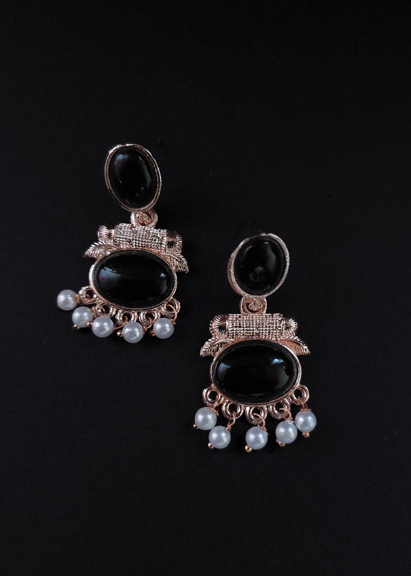 Pair of earrings with black stones and pearl-like beads on a black background