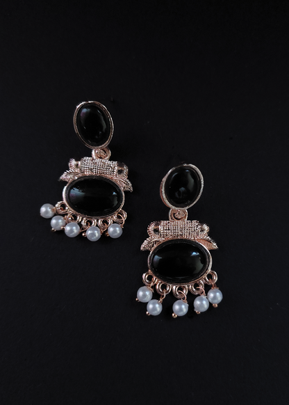 Pair of earrings with black stones and pearl-like beads on a black background