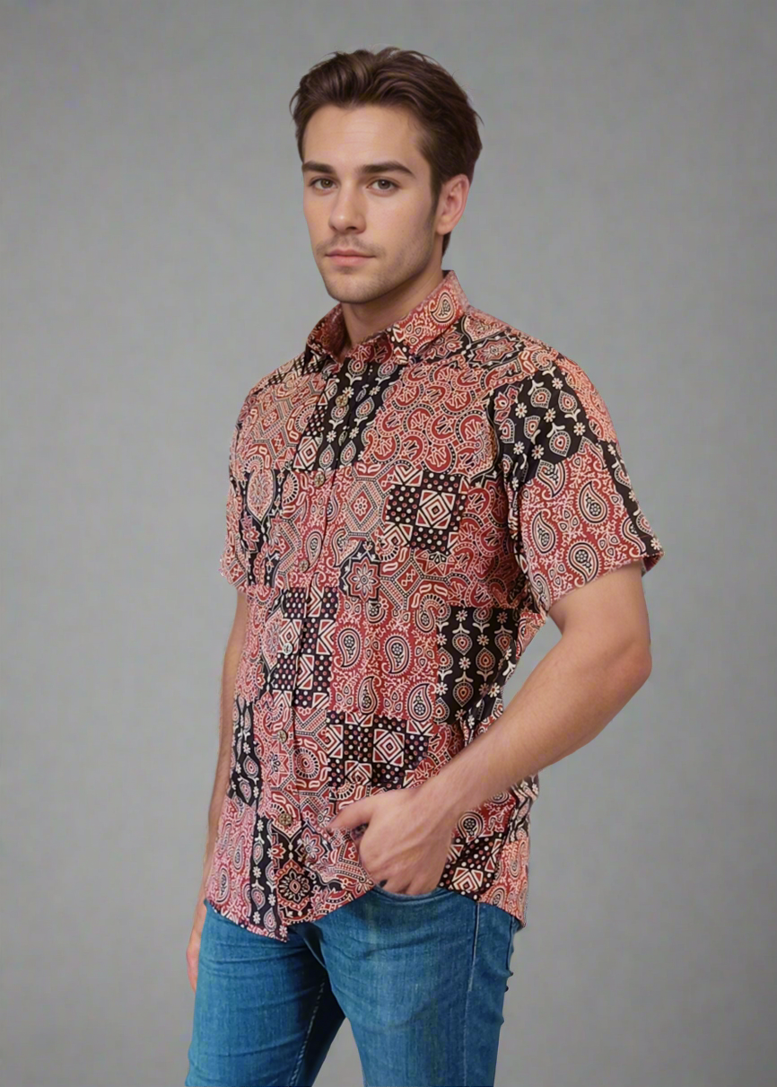 Man wearing a patterned shirt and blue jeans on a plain background