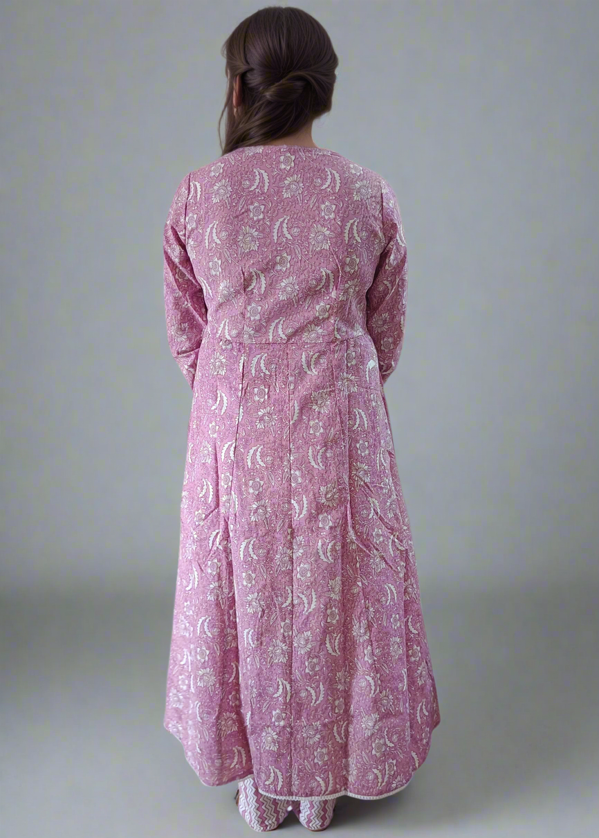 Person wearing a long pink dress with white patterns on a plain background