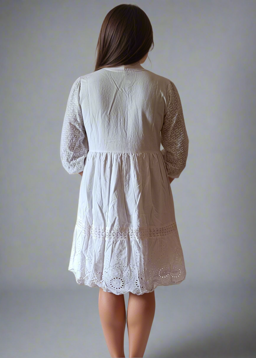 Woman wearing a white dress with lace details against a plain background