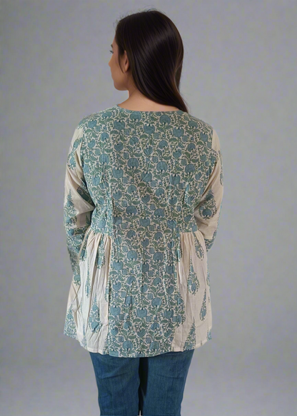 Woman wearing a patterned flroral paisley top and jeans on a plain background