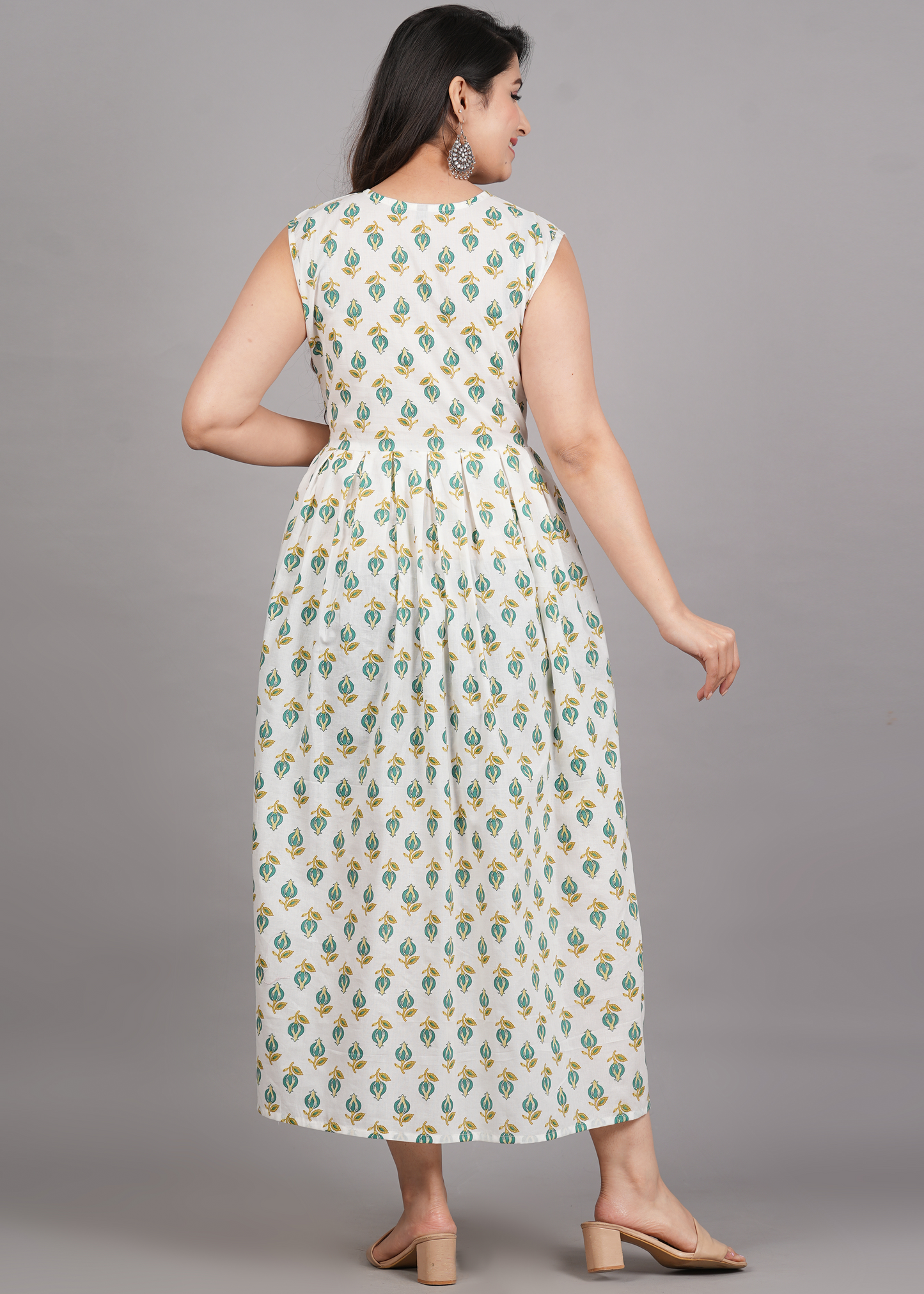 A woman modeling a sleeveless, knee-length white maxi dress with a green and yellow floral block print, shown from the back against a solid gray studio background.