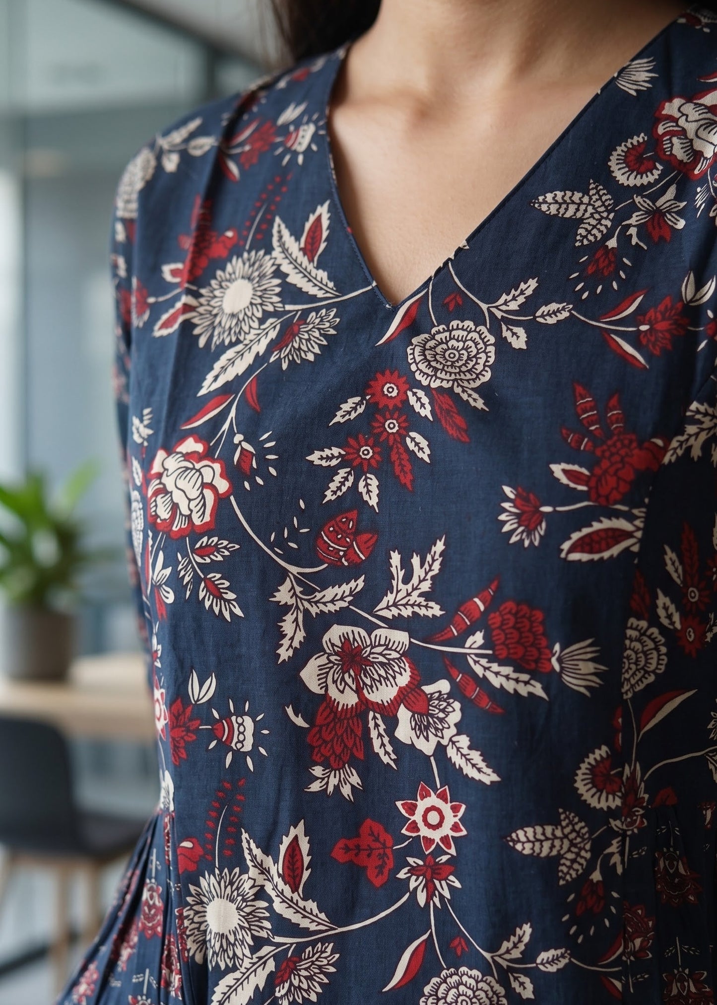 A close-up of a person wearing a navy blue V-neck short kurti with a red and cream floral pattern, paired with blue jeans.