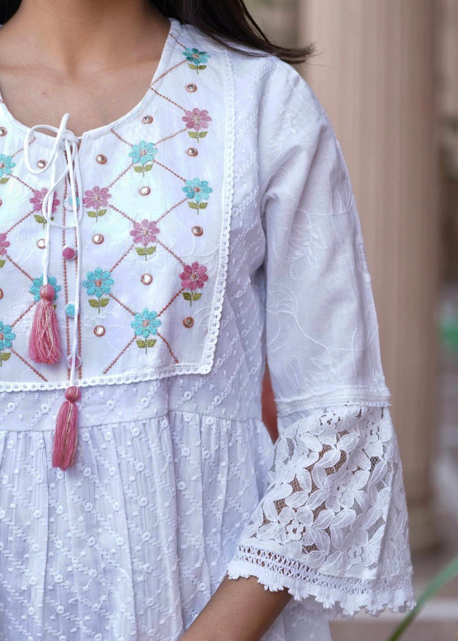 White embroidered dress with floral patterns and tassels on a blurred background