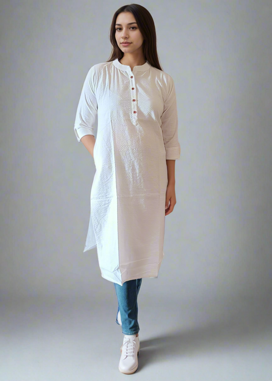 Woman wearing a white kurta with blue jeans against a plain background