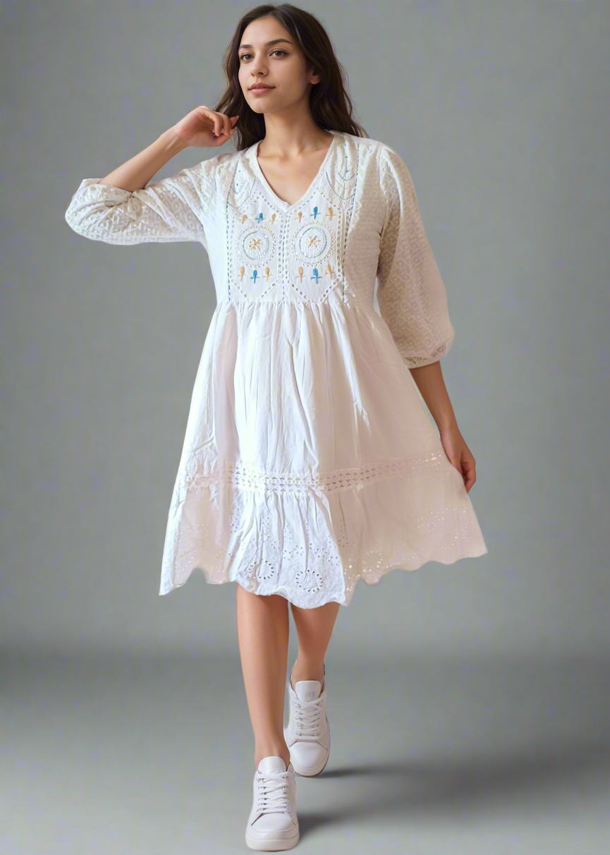 Woman wearing a white dress with embroidery on a plain background