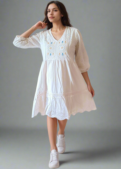 Woman wearing a white dress with embroidery on a plain background