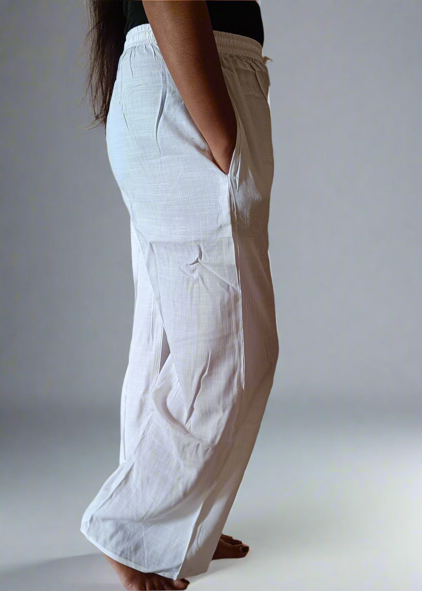Person wearing white pants standing against a plain wall.