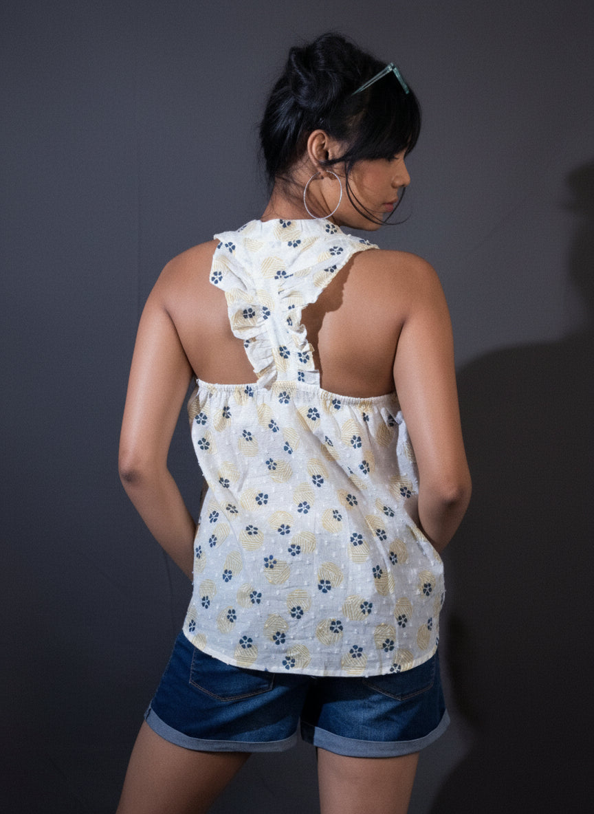 Woman wearing a white floral halter top and blue shorts standing against a dark curtain.