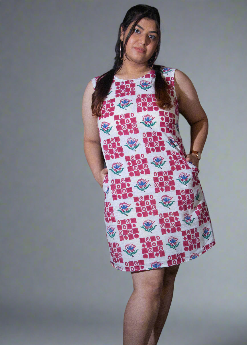 Woman wearing a patterned dress standing against a dark background with a plant to her left.