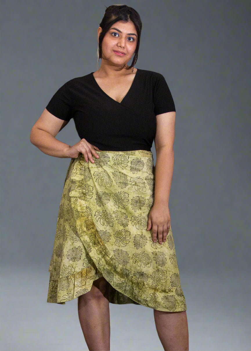 Person wearing a black top and green patterned wrap skirt against a plain background