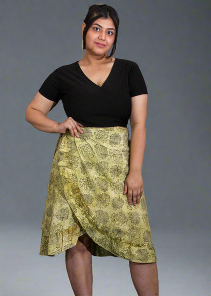 Person wearing a black top and green patterned wrap skirt against a plain background