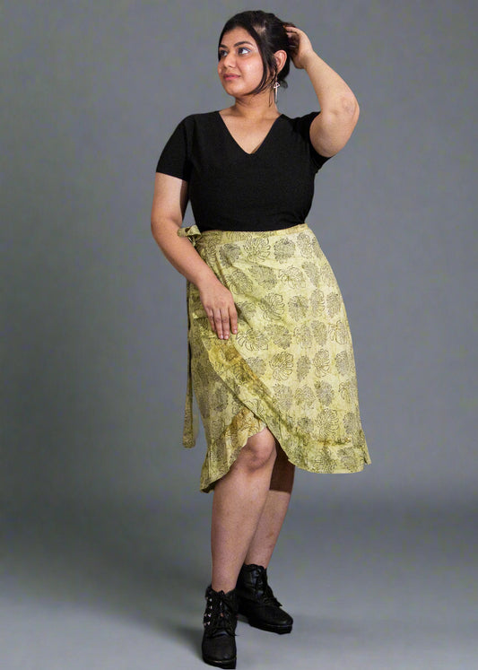 Woman wearing a black top and green patterned wrap skirt against a plain background