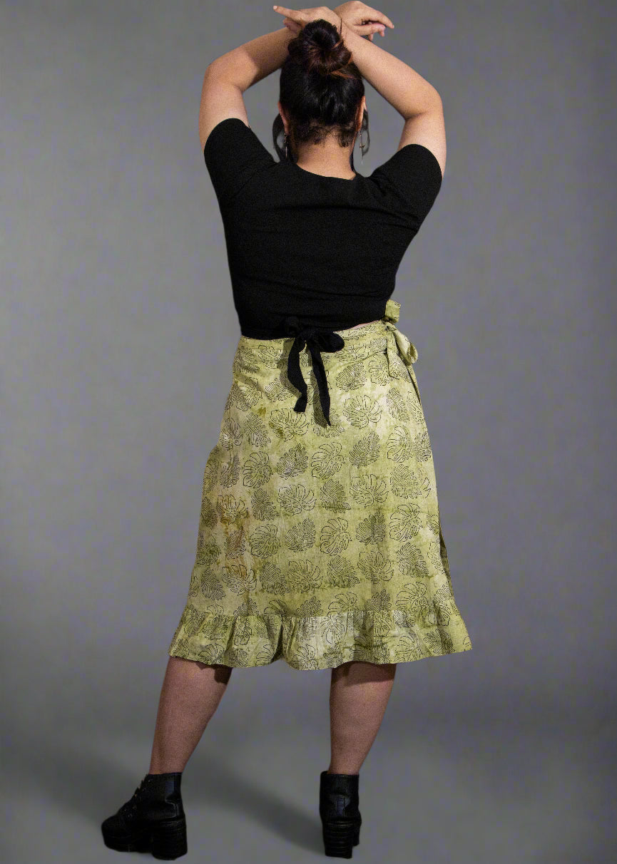 Person wearing a black top and green patterned wrap skirt against a dark background