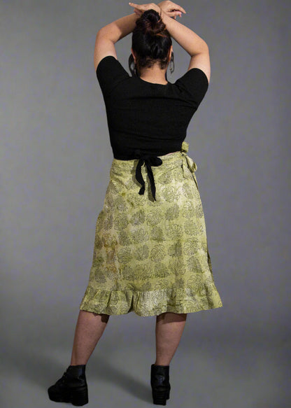 Person wearing a black top and green patterned wrap skirt against a dark background