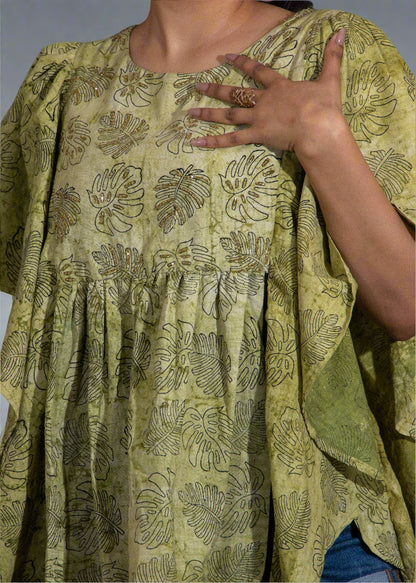 Person wearing a green patterned tropical top with a blurred background