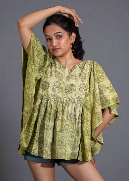 Woman wearing a green patterned flared top and denim shorts against a dark background