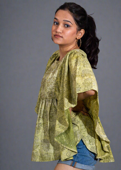 Woman wearing a green patterned top and denim shorts against a dark background