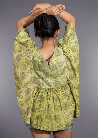 Person wearing a green patterned top with half sleeves and shorts against a black background