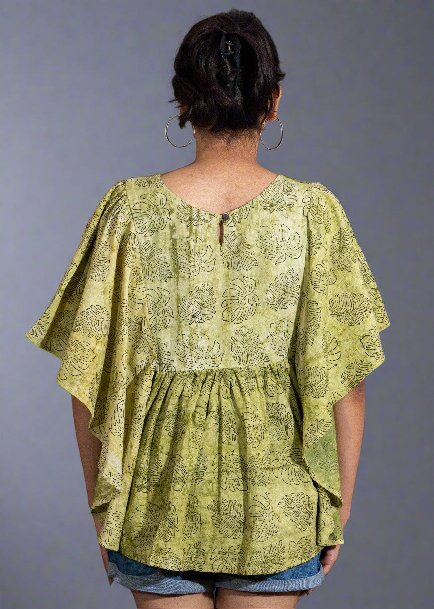 Person wearing a green patterned blouse with short sleeves against a dark background