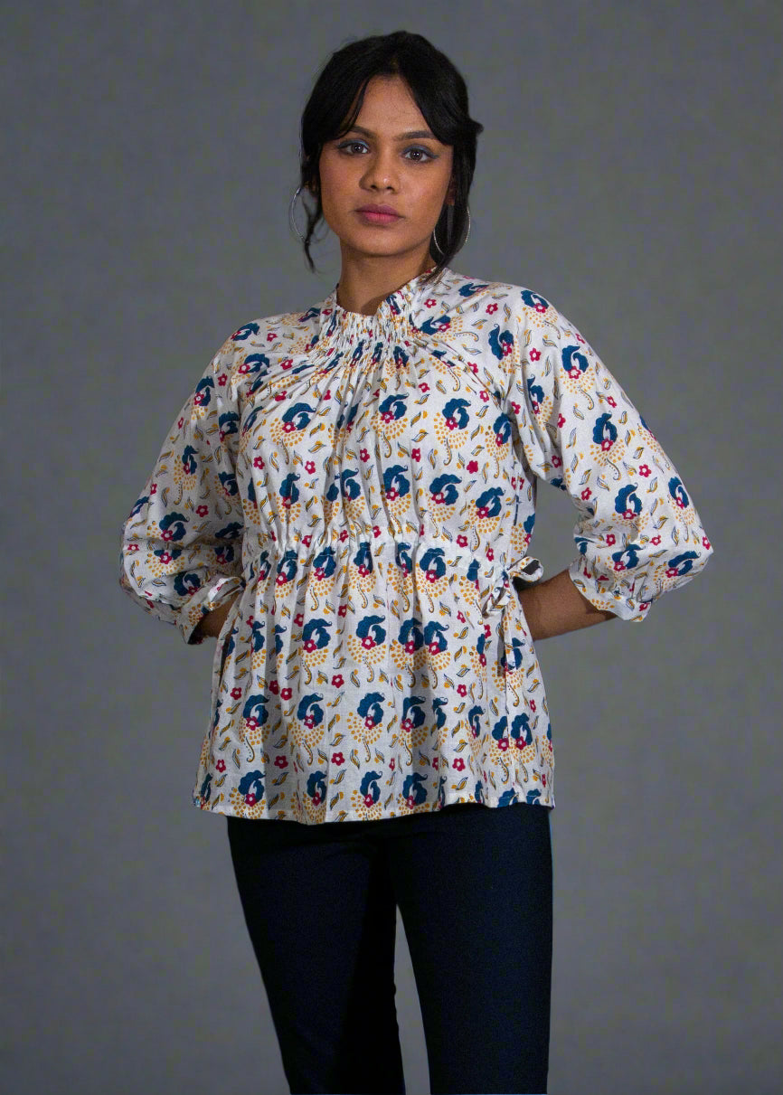 Woman wearing a patterned blouse and black pants against a plain background