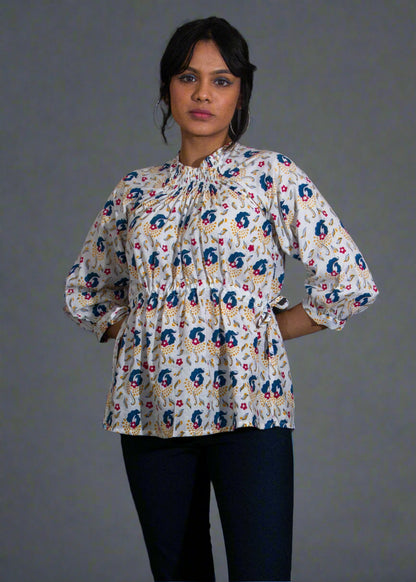 Woman wearing a patterned blouse and black pants against a plain background