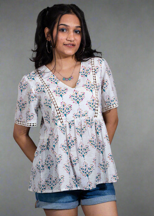 Woman wearing a white floral blouse and denim shorts against a dark background