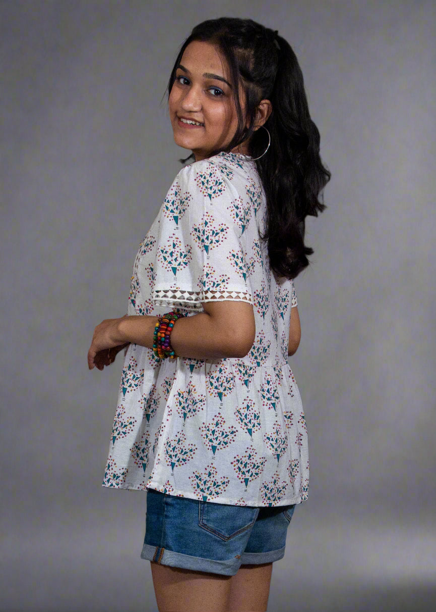 Woman wearing a white floral top and blue shorts against a black background