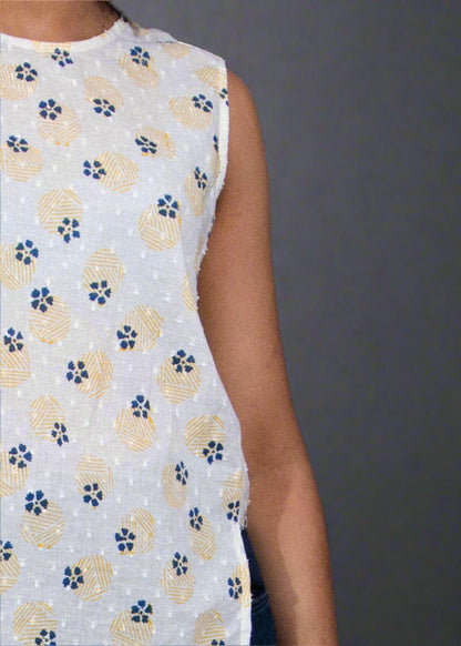 Woman wearing a white sleeveless top with floral pattern and blue jeans against a black background