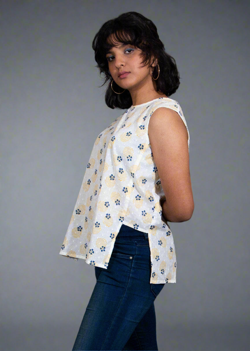 Woman wearing a sleeveless floral top and dark jeans against a black background