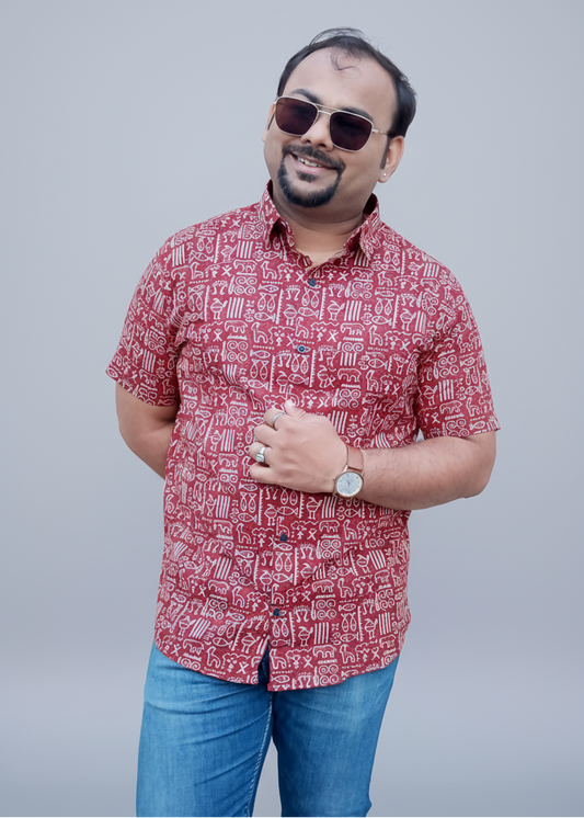 Man wearing a red patterned shirt and blue jeans against a plain wall.